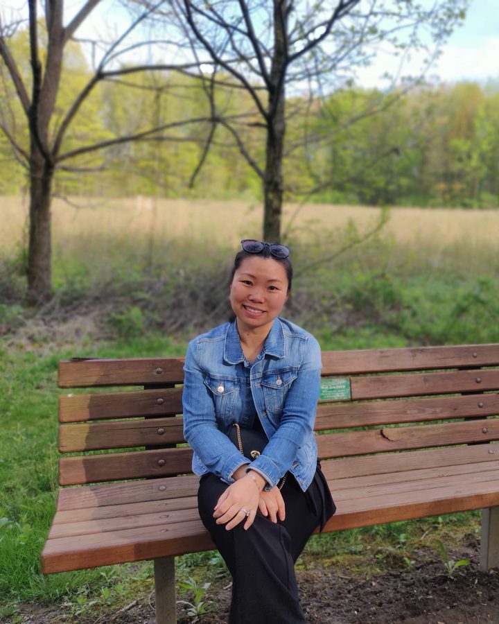 Teacher Penny seated on a park bench, smiling
