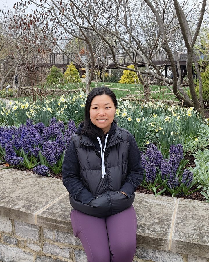 Teacher Penny smiling in a garden of spring flowers